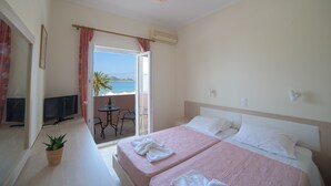 A hotel room with two beds, a TV, a potted plant, and a balcony with a table and chairs. - Alkyon Beach Hotel (Corfu)