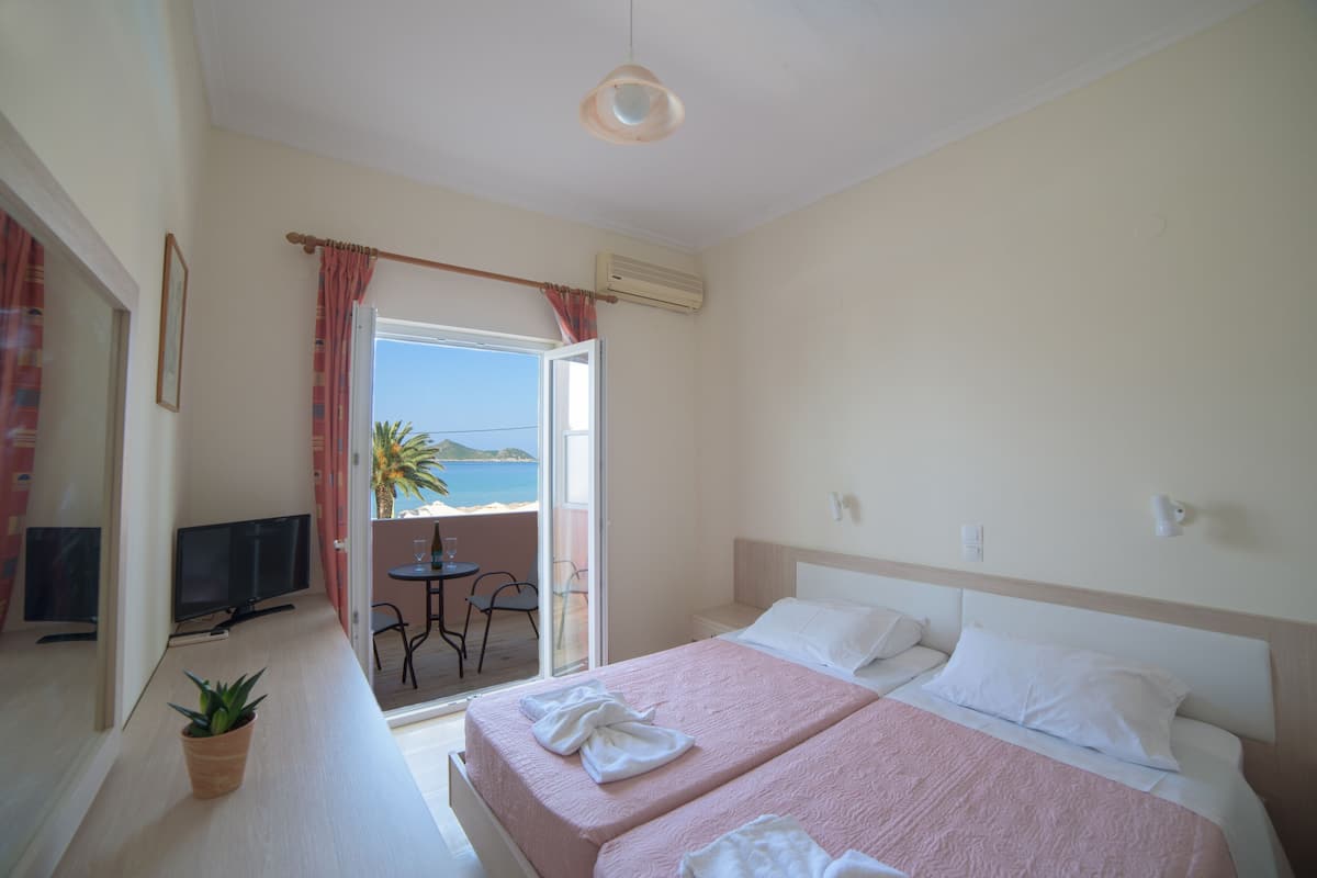 A hotel room with two beds, a TV, a potted plant, and a balcony with a table and chairs.