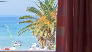 A table with a bottle and glasses, a view of the sea, palm trees, and a red curtain. - Alkyon Beach Hotel (Corfu)