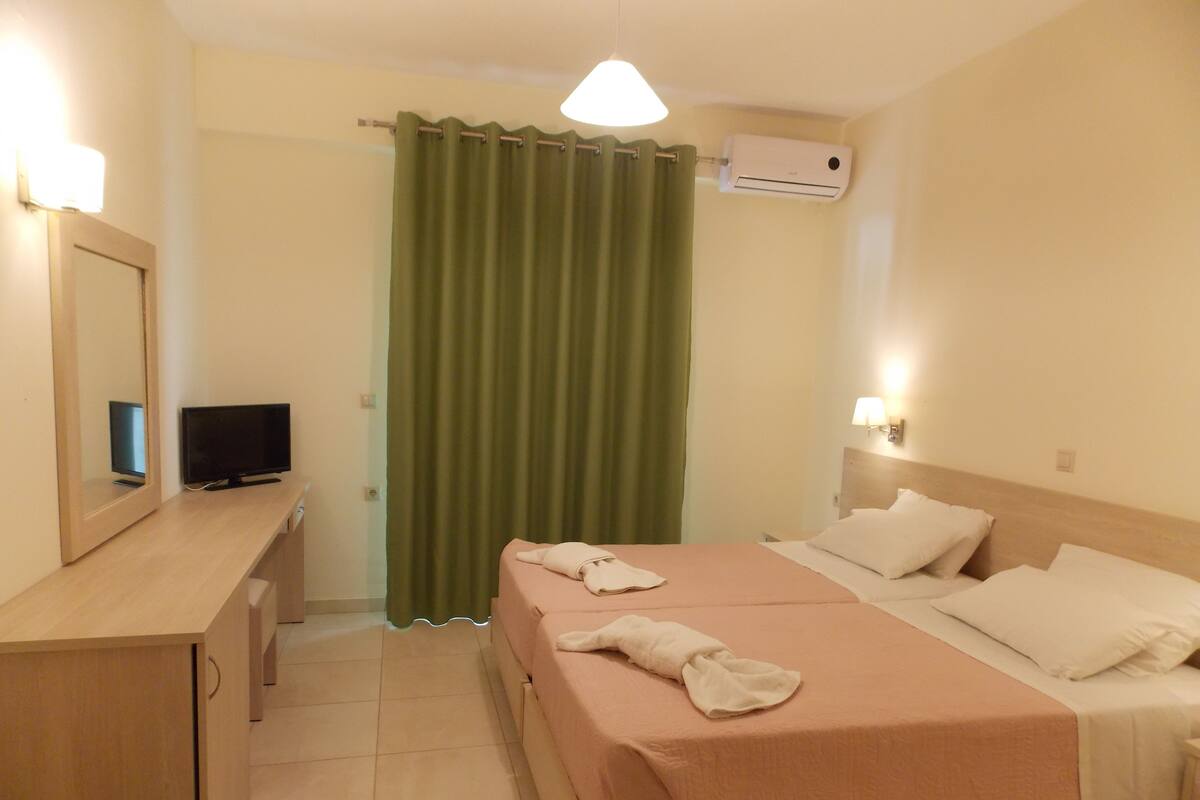A hotel room with a bed, a television, a desk, and a curtain.