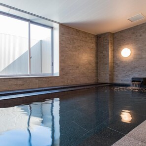 Una piscina interior amplia con vistas despejadas al cielo a través de grandes ventanales, diseño moderno con pared de piedra y una lámpara redonda en la pared.