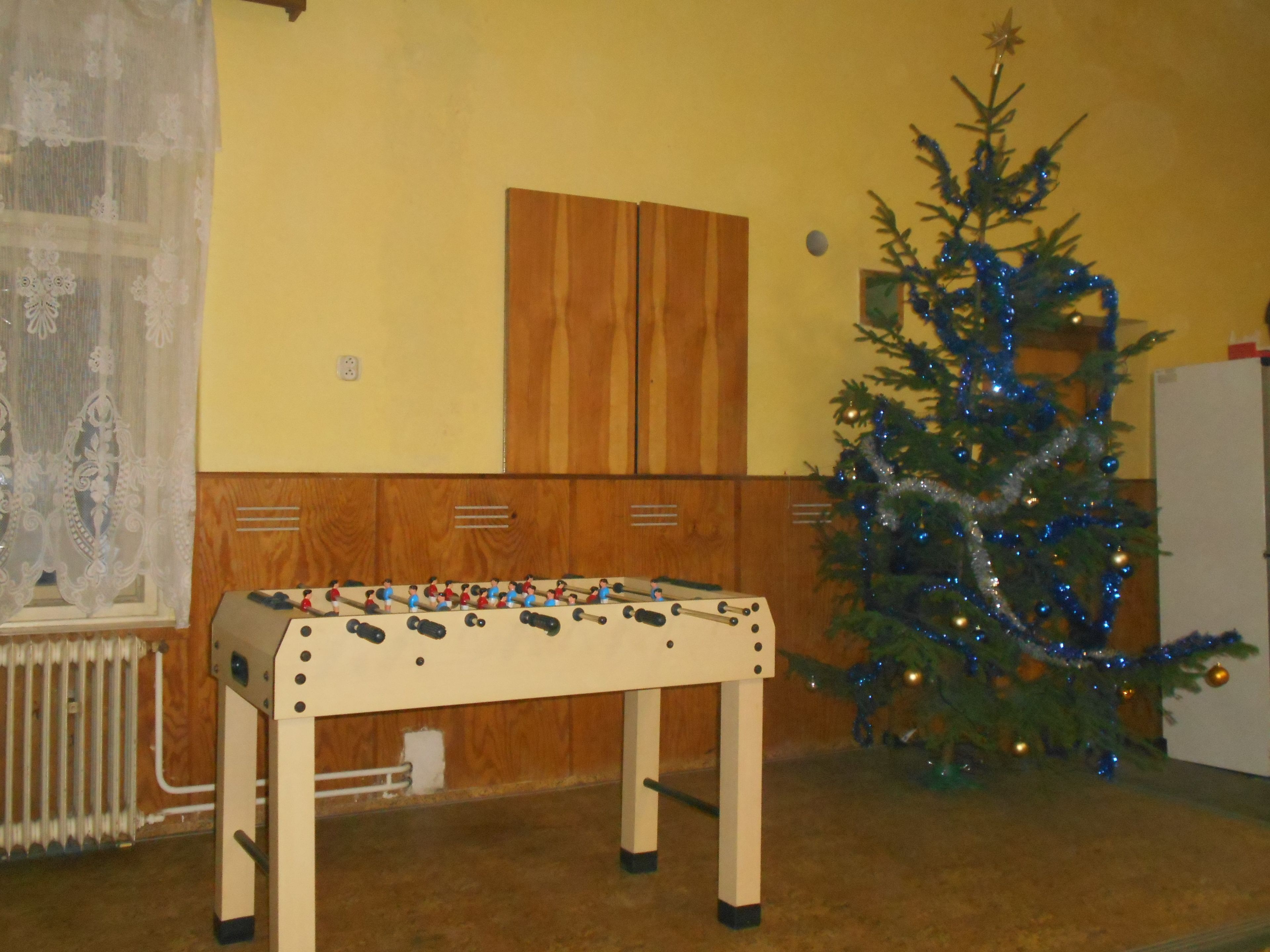 Een kamer met een houten kast, een tafelvoetbalspel en een kerstboom met lichtjes.