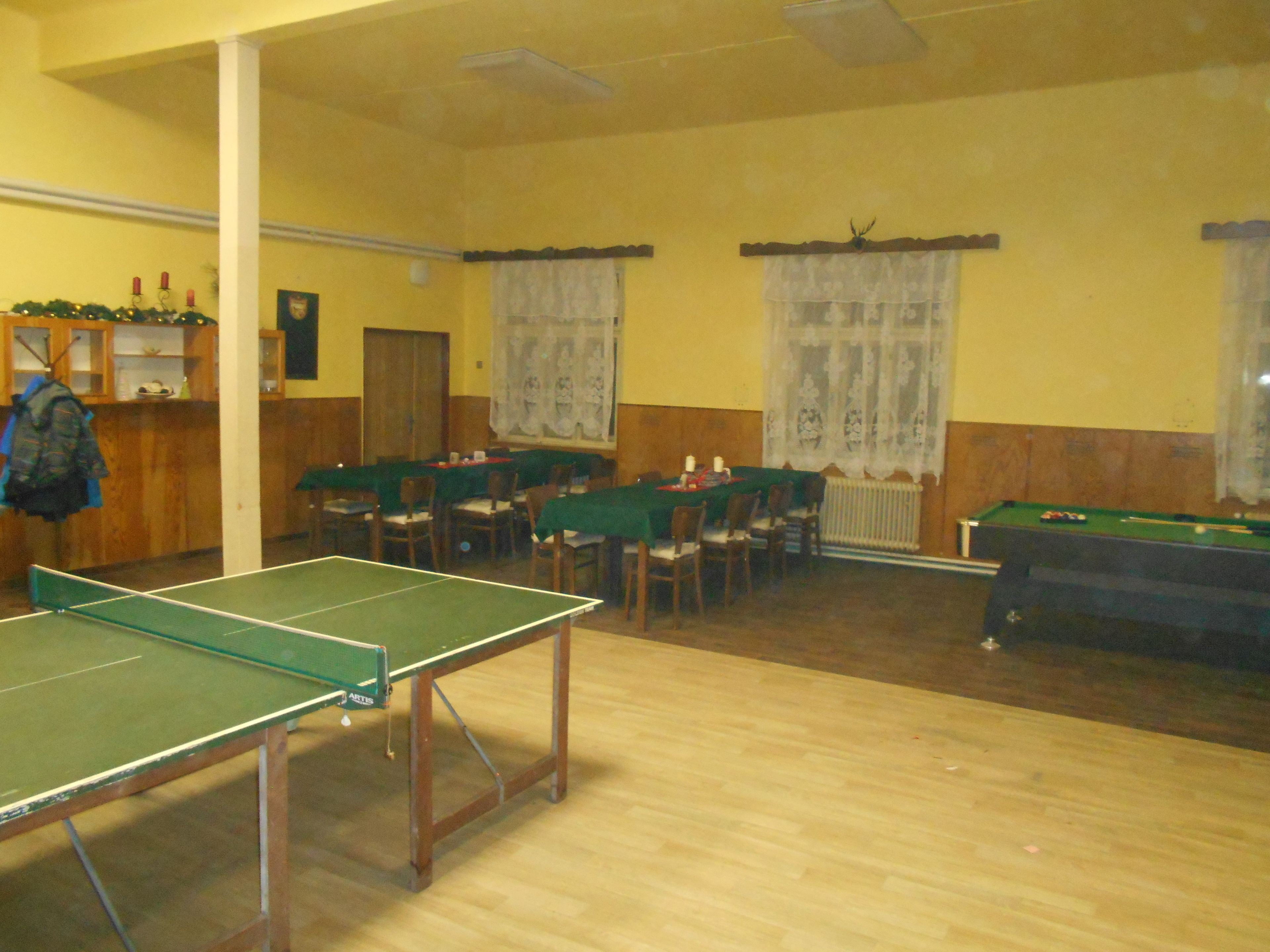 A room with a ping pong table, pool table, and several dining tables with chairs.