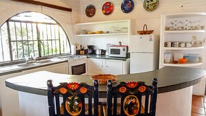 Una cocina con una isla central, armarios blancos y un microondas. Hay platos decorativos en la pared y una ventana con vistas a zonas verdes.