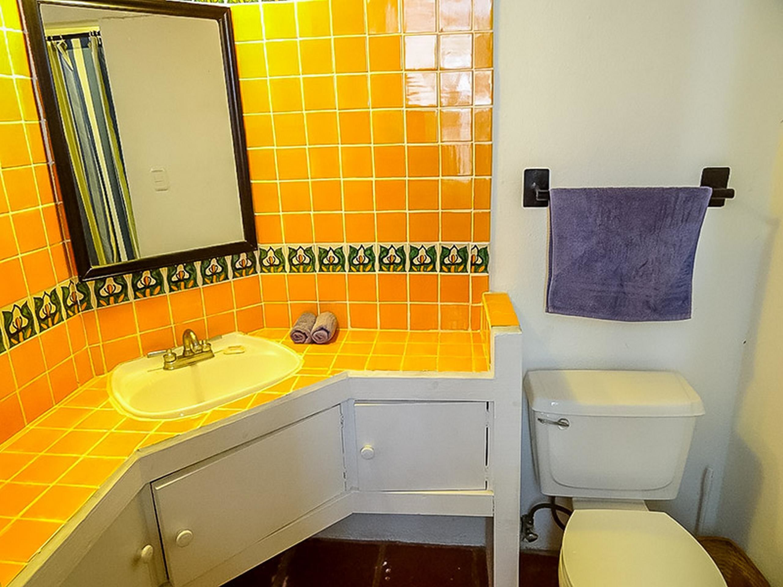 A bathroom with a yellow tiled wall, a white sink, a white toilet, and a towel hanging on a hook.