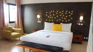 A hotel room with a bed, a bedside table, a chair, and a wall with geometric patterns. - Douala Design Hotel (Douala)