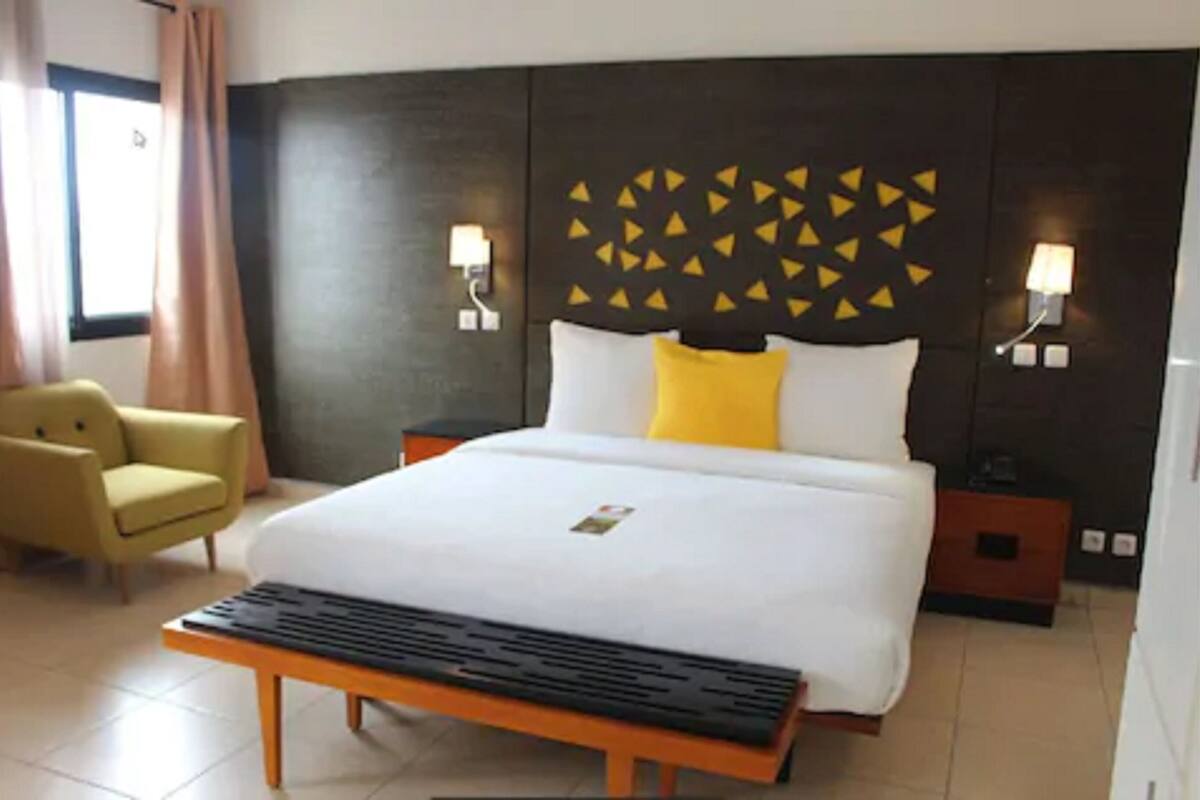 A hotel room with a bed, a bedside table, a chair, and a wall with geometric patterns.