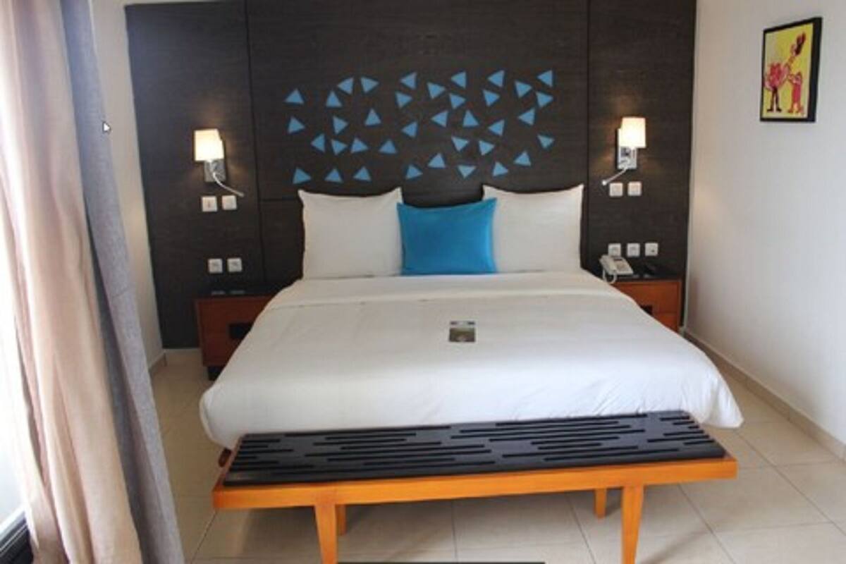 A hotel room with a bed, a bedside table, a nightstand, a wall-mounted light, and a picture on the wall.