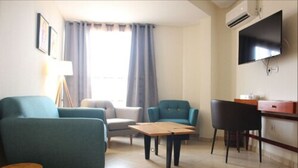 A living room with teal sofas, a wooden coffee table, and a TV mounted on the wall. - Douala Design Hotel (Douala)