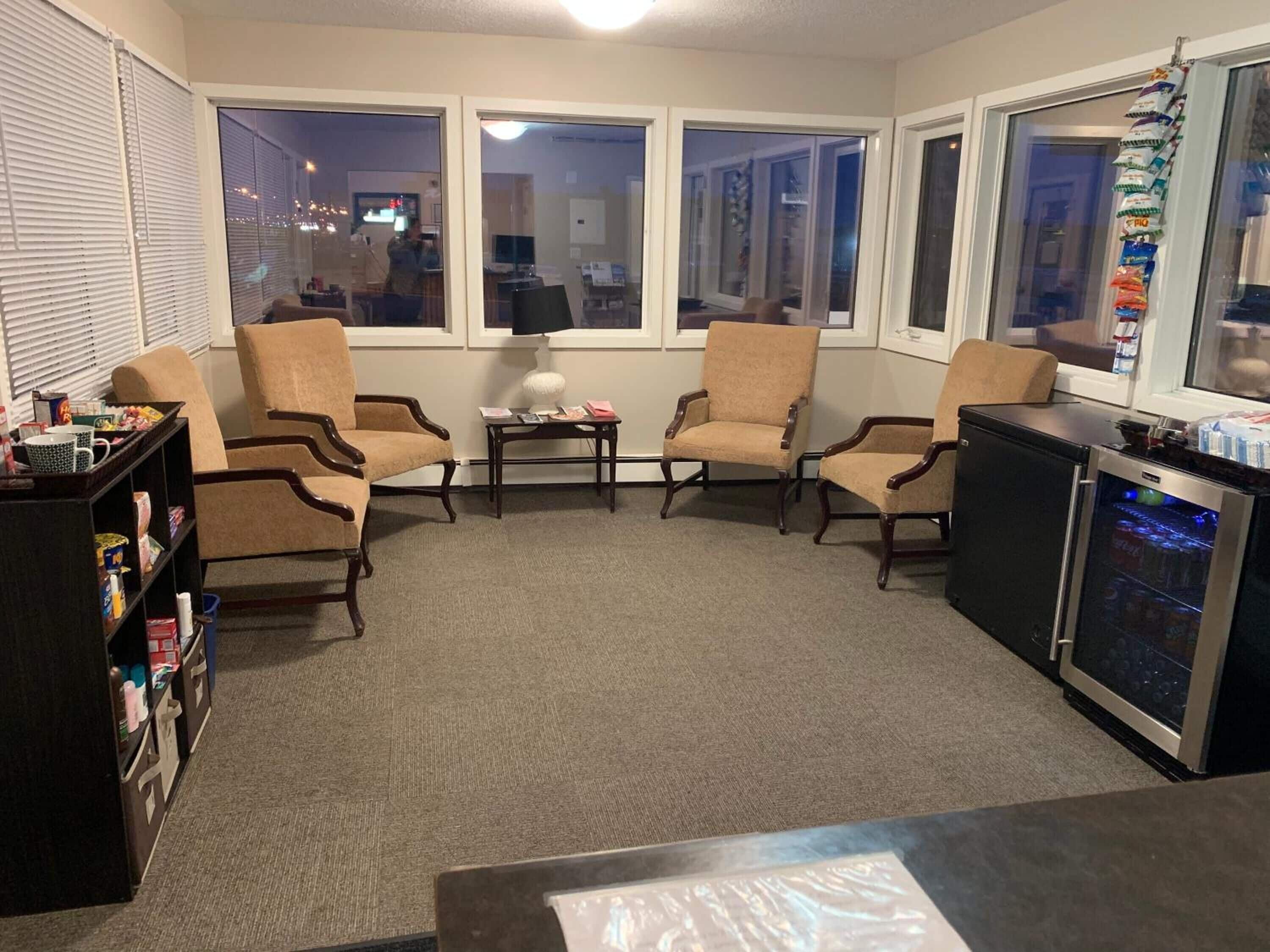 A living room with four armchairs, a coffee table, a bookshelf, and a refrigerator.