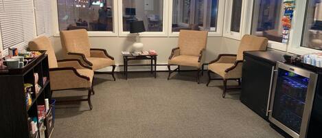 A living room with four armchairs, a coffee table, a bookshelf, and a refrigerator.