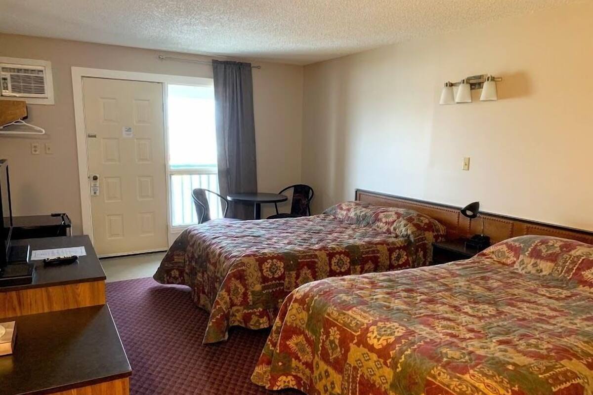 Quarto de hotel com duas camas, uma escrivaninha, uma cadeira e uma mesinha.