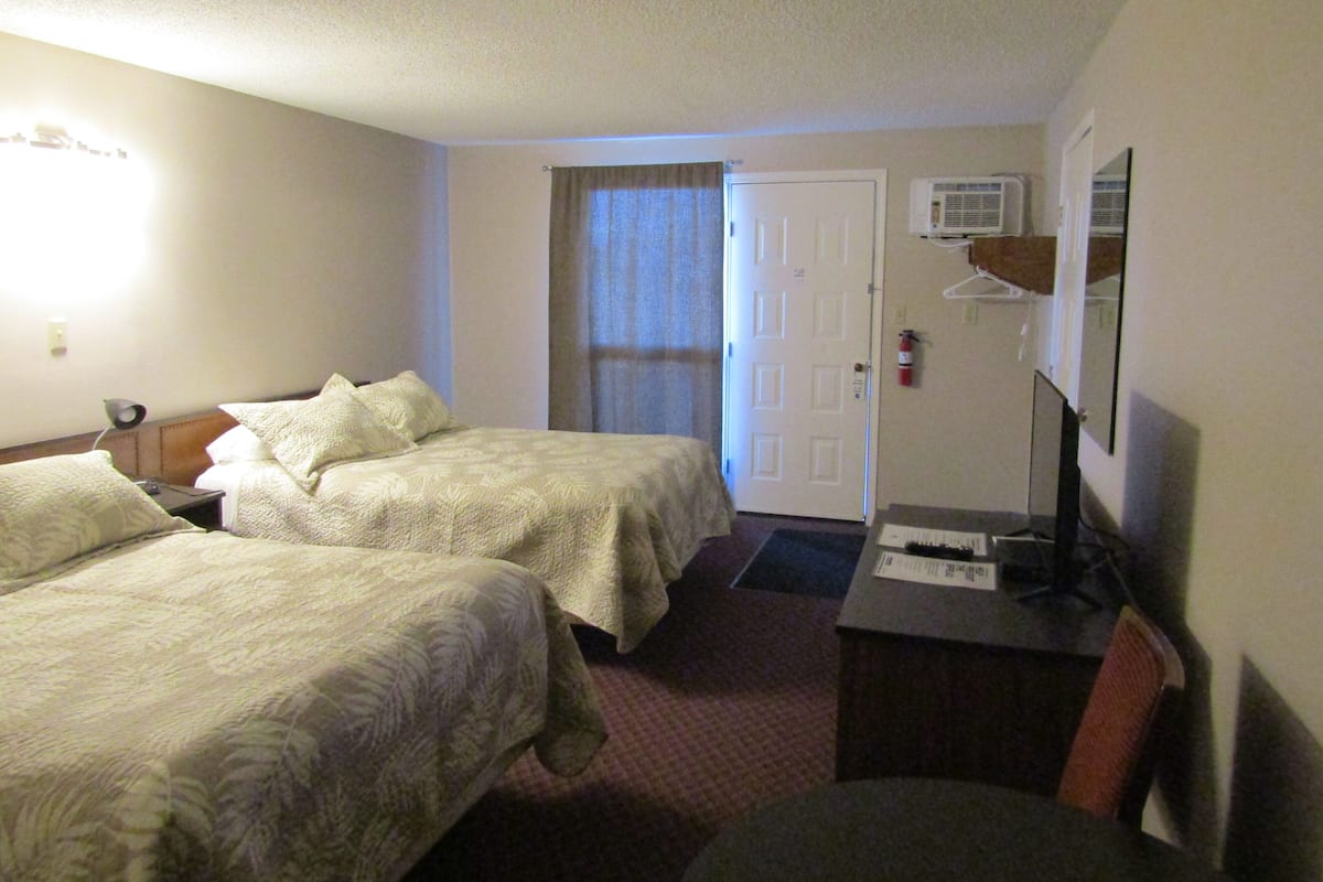 Quarto de hotel com duas camas, uma escrivaninha, uma cadeira, uma televisão e uma porta.