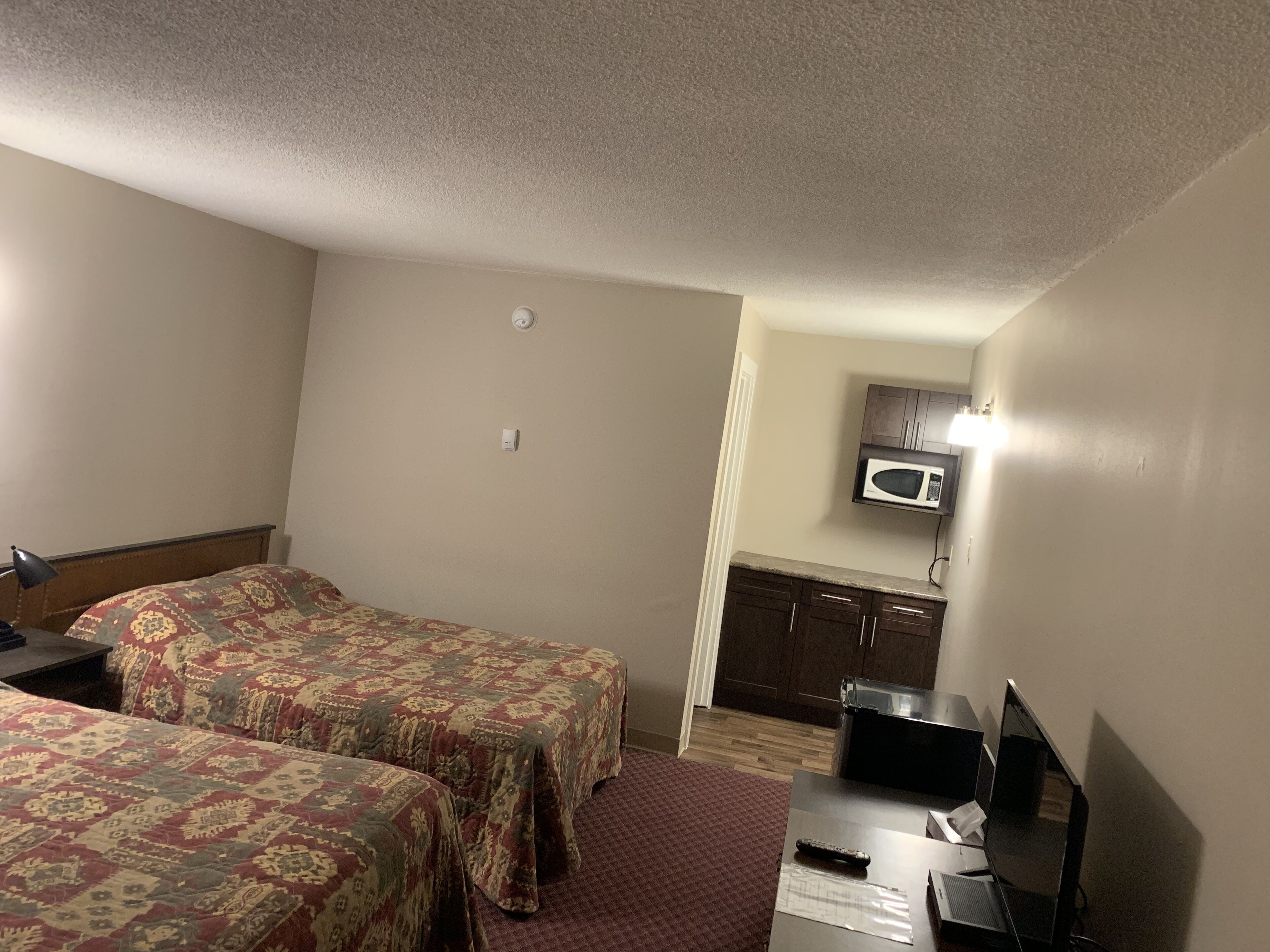 A hotel room with two beds, a desk with a computer, a microwave, and a small kitchenette.