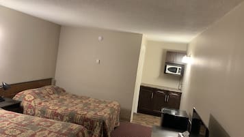 A hotel room with two beds, a desk with a computer, a microwave, and a small kitchenette.