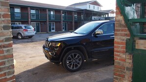 Een zwarte SUV geparkeerd voor een gebouw met een bakstenen gevel en groene reling.