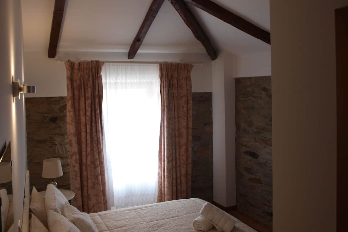 Ein Schlafzimmer mit Steinwand, einem Bett mit weißen Leinen und einem Fenster mit Vorhängen.