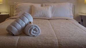 Een net opgemaakt bed met een opgerolde witte handdoek en een kleine potplant ernaast.