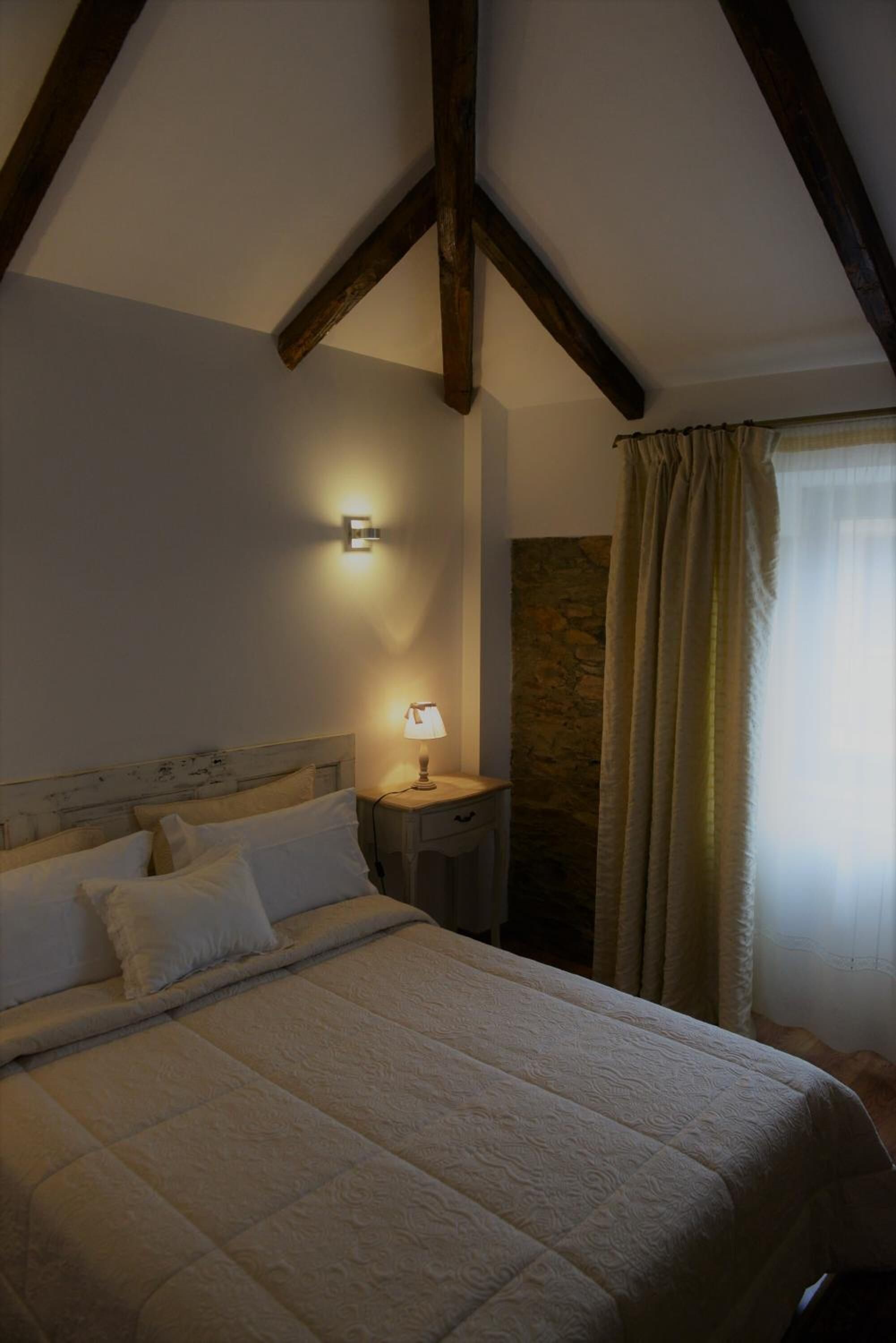 Un dormitorio con una cama grande, una mesita de noche, una lámpara de pared y una pared de piedra.