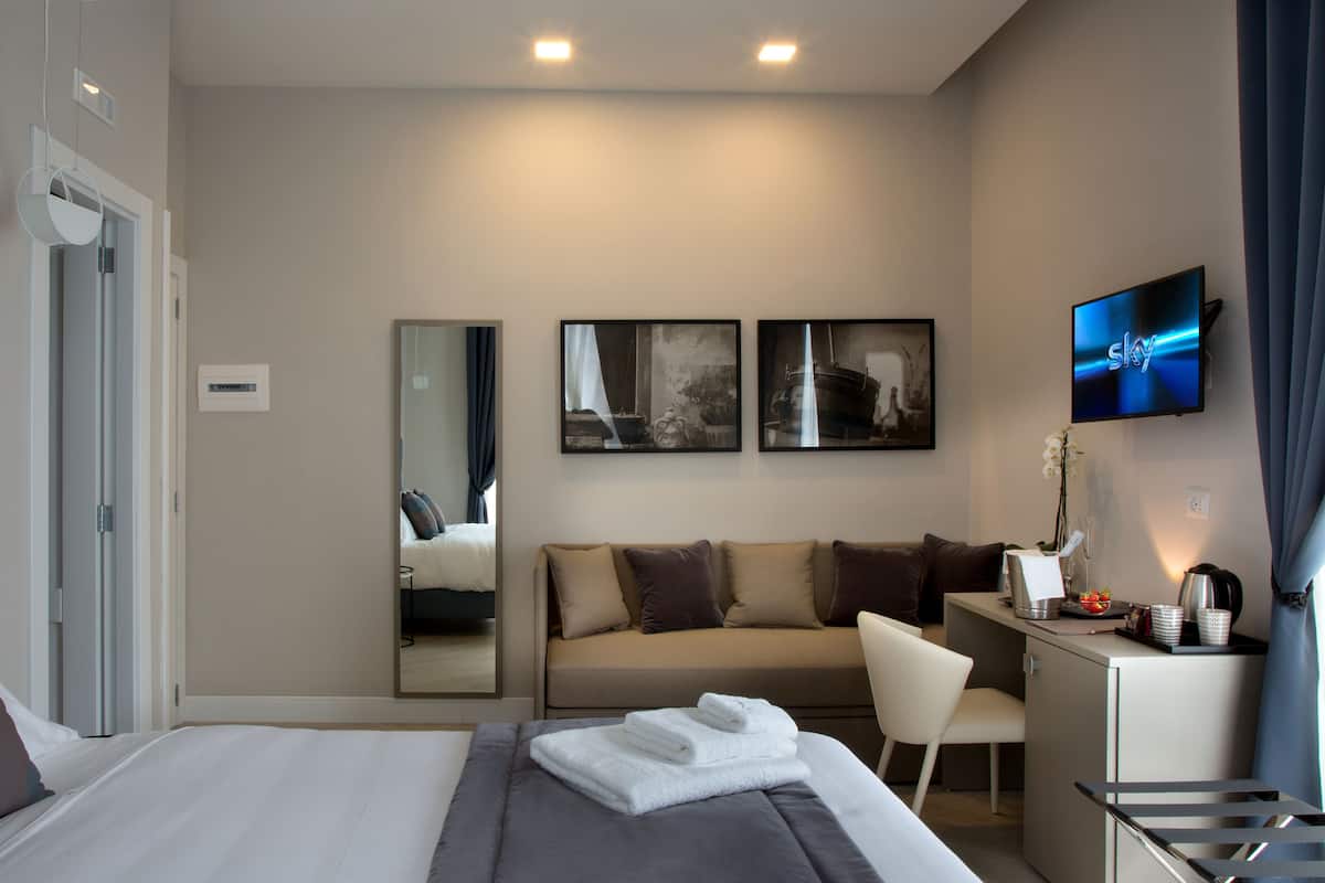 A modern hotel room with a bed, a sofa, a desk, and a TV.