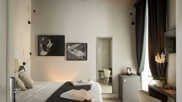 Ein modernes Hotelzimmer mit Bett, Schreibtisch, Stuhl, kleinem Kühlschrank und einer Topfpflanze.