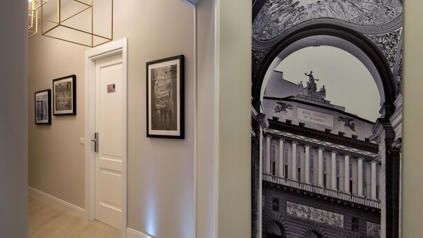 Un corridoio con fotografie in bianco e nero incorniciate alle pareti, una porta bianca e un arco decorativo con rilievo scolpito.