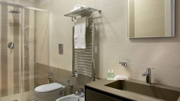 Un baño moderno con cabina de ducha de vidrio, inodoro, bidé, lavabo y perchero para toallas.