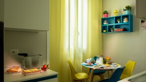 Zona pranzo con tavolo apparecchiato per due, un tostapane e una ciotola di frutta.