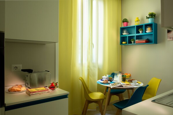 A dining area with a table set for two, a toaster, and a bowl of fruit.