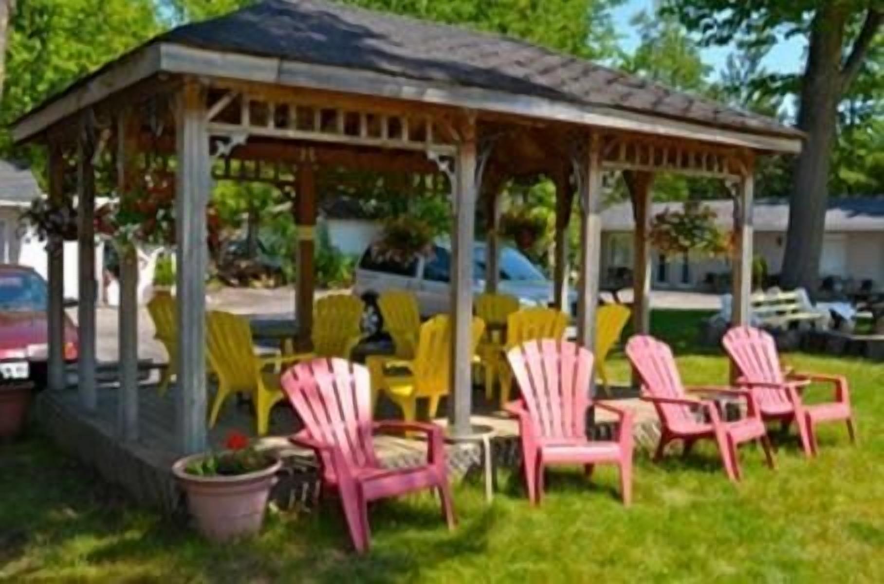 Un espace extérieur aménagé, abrité et doté de chaises et de tables, entouré de verdure.
