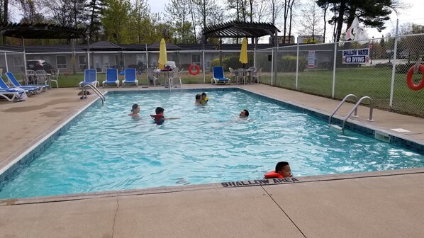 A swimming pool with a shallow water area marked, surrounded by lounge chairs and a fenced area with a sign indicating no diving. - Wasaga Beach Inn And Cottages (Wasaga Beach)