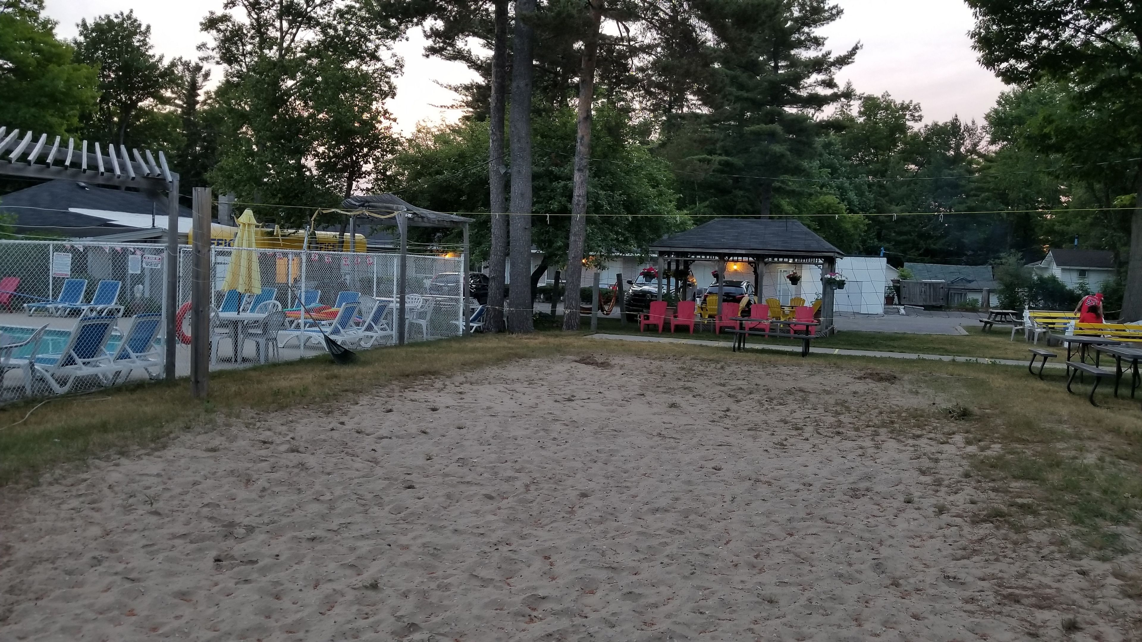 Un espacio al aire libre cercado con superficie de arena, mesas y sillas de picnic.