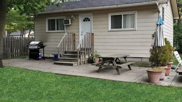 Une maison de plain-pied avec un porche à l’avant, un barbecue et une table de pique-nique.