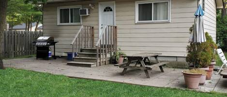 A single-story house with a front porch, a barbecue grill, and a picnic table.