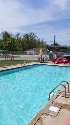 A clear swimming pool with a lifebuoy, a fenced area, and a covered seating area with chairs. - Wasaga Beach Inn And Cottages (Wasaga Beach)