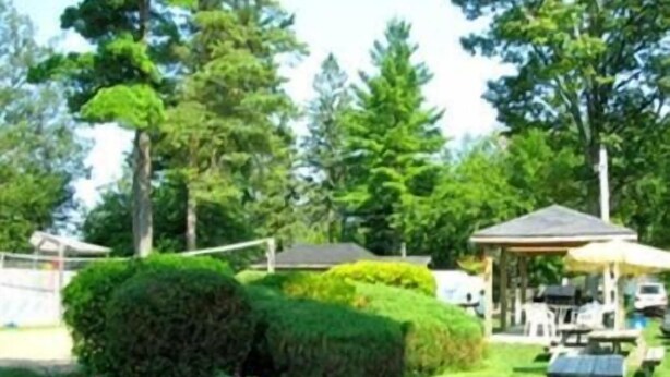 Ein gepflegter Garten mit einem Laube, Picknicktischen und ordentlich geschnittenen Hecken.