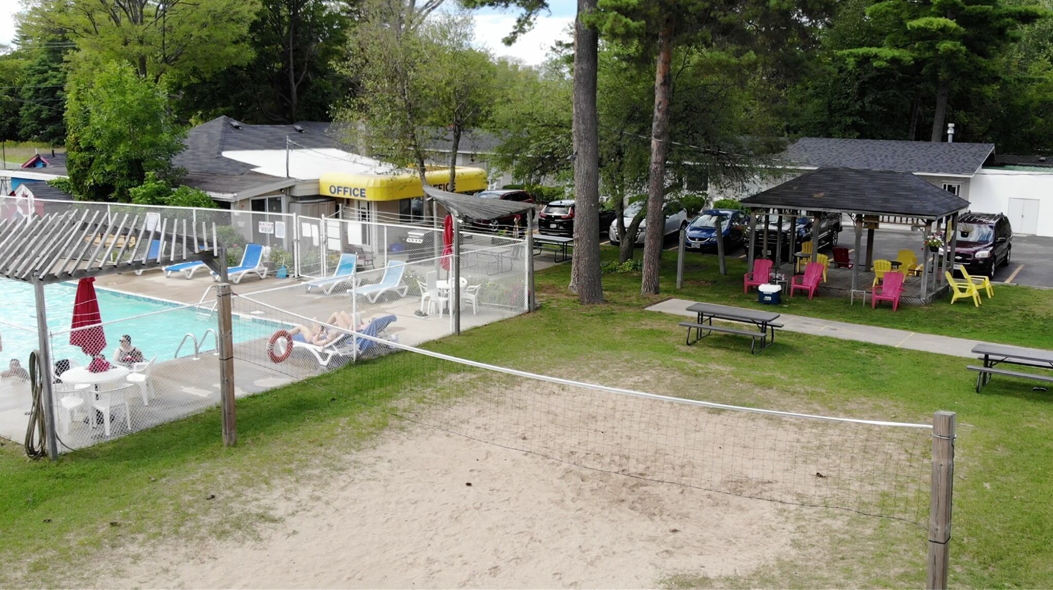 Un espace piscine doté d’une terrasse entourée d’une clôture, de chaises longues et d’un coin salon couvert avec des tables et des chaises.