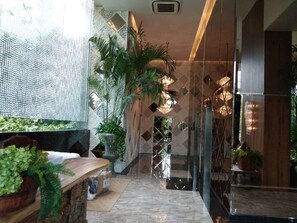A modern hotel lobby with a glass partition, potted plants, and a marble floor.