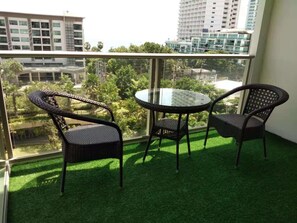 A balcony with artificial grass, two wicker chairs, and a glass table.
