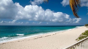 Een strand met helder turquoise water, wit zand en een houten balustrade.