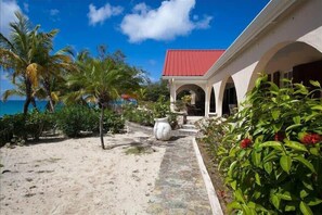 Uma propriedade à beira-mar com um edifício de telhado vermelho, um caminho de areia e vegetação tropical.