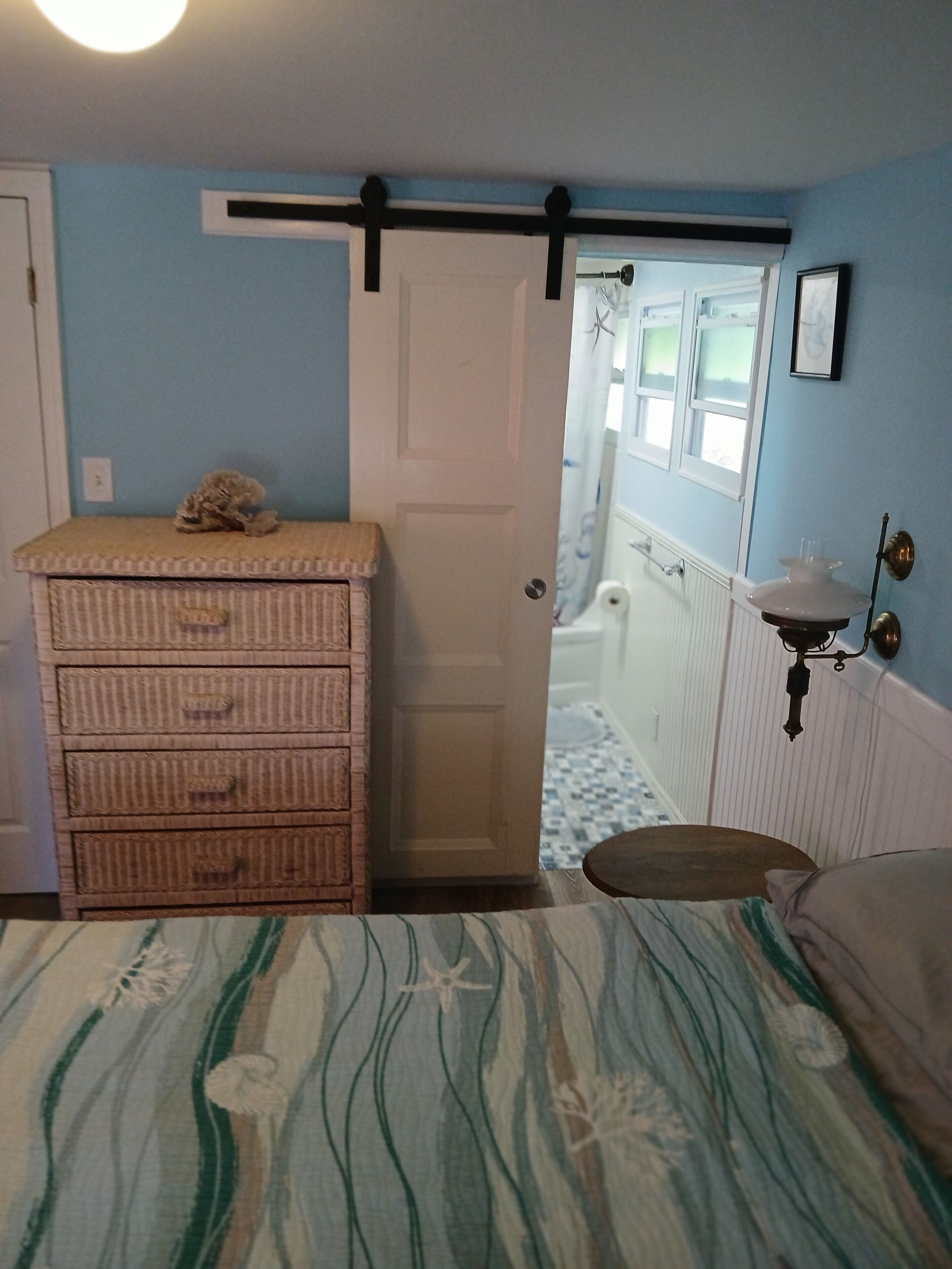 Une chambre à coucher avec un lit, une commode, une porte, une fenêtre et une salle de bain visible à travers la porte.