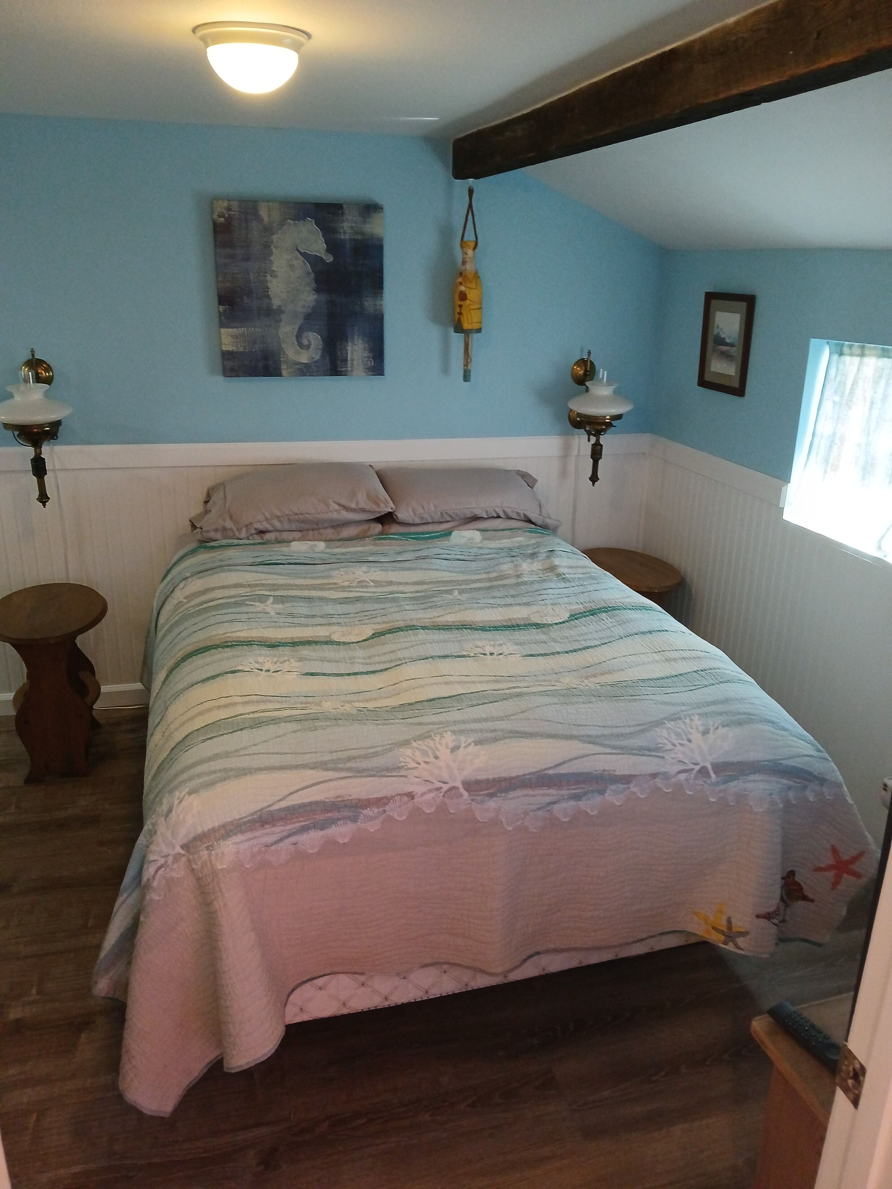 Un dormitorio con una cama, dos mesitas de noche, una lámpara de pared, un cuadro y una ventana.