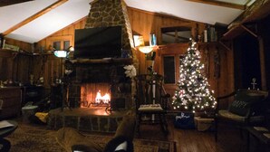 A cozy room with a stone fireplace, wooden beams, a Christmas tree, and a television.