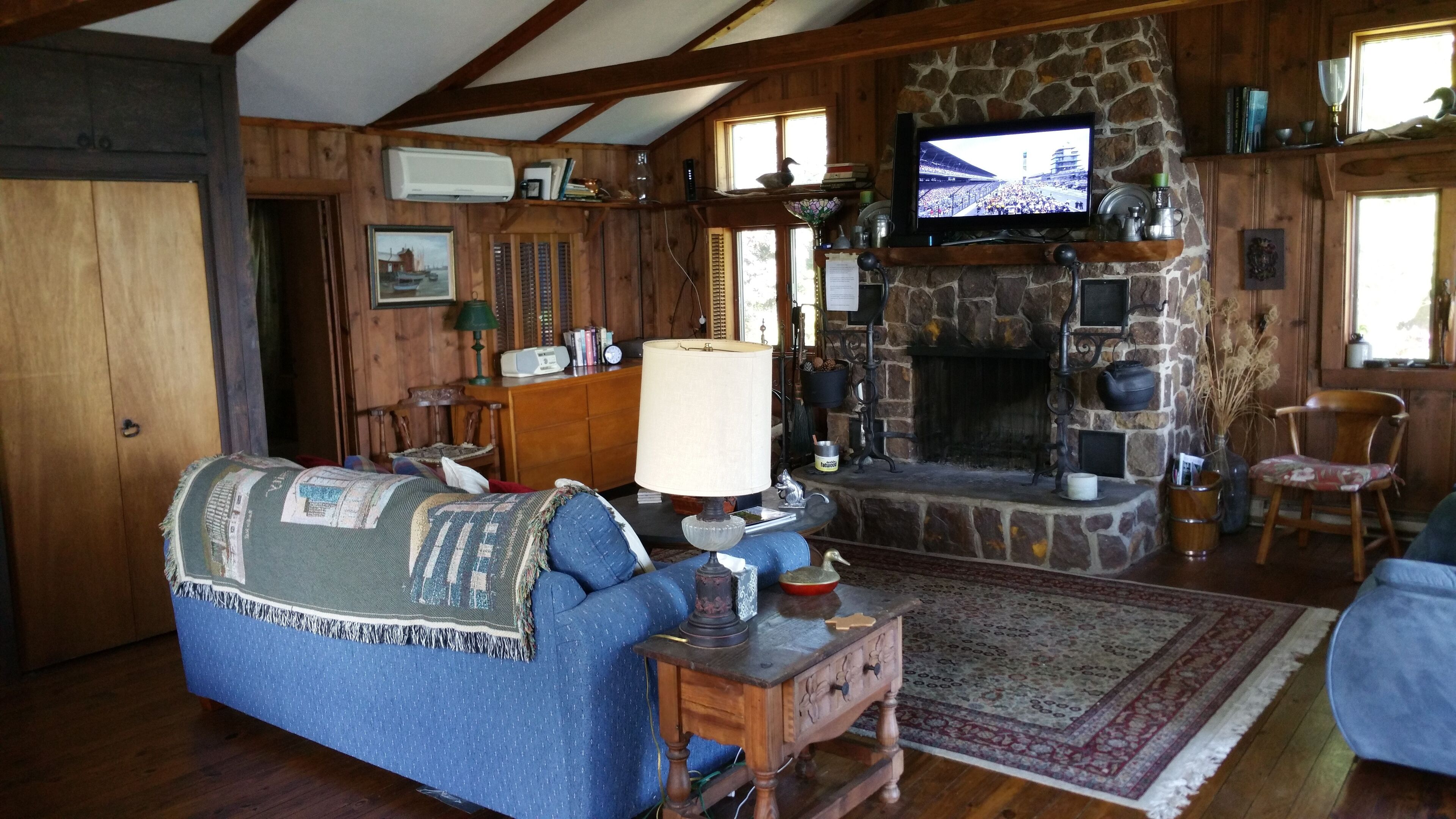Una sala de estar acogedora con chimenea de piedra, paredes de madera, un televisor montado encima y un sofá azul.