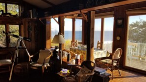 A cozy room with a telescope, chairs, a table, and a view of the sea.