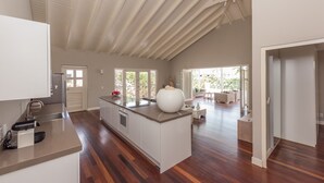 Een ruime keuken met een groot eiland, houten vloeren en uitzicht op het betegelde terras.