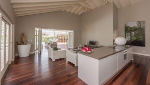 Een ruime keuken met een groot eiland, een eethoek met rieten meubels en uitzicht op een buitenzwembad.