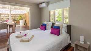 Een hotelkamer met een groot bed, een houten vloer, een tafeltje met een stoel, en een raam met uitzicht op groen.