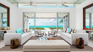 Ein geräumiges Wohnzimmer mit einem großen weißen Sofa, zwei Sesseln und einem Couchtisch. Das Zimmer verfügt über große Glasüren, die auf einen Balkon mit Meerblick führen.
